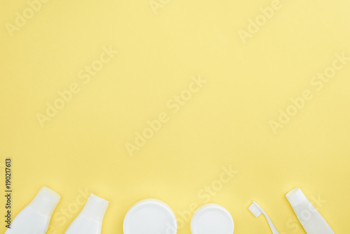 top view of plastic containers and bottles with cream, toothpaste and toothbrush, isolated on yellow