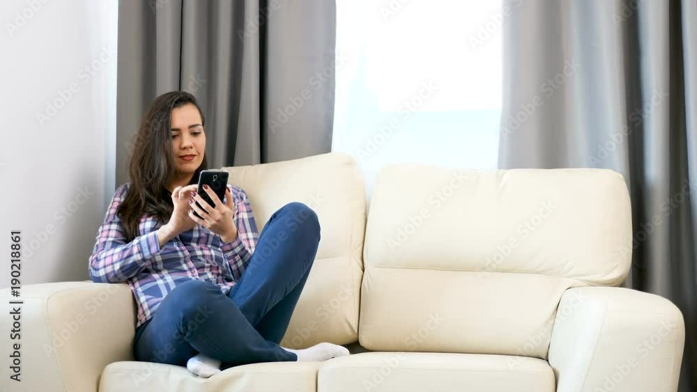 Woman relaxing on the couch and browsing through her smarphone Woman relaxing on the couch and browsing through her smarphone