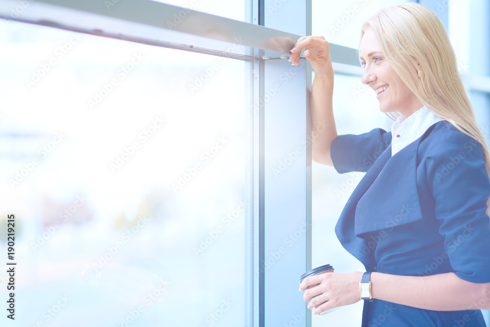 Businesswoman standing against office window holding laptop. Businesswoman