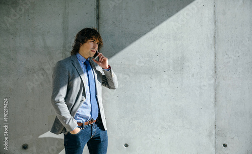 Businessman talking on the cell phone in front of a concrete wall