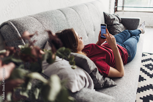 Young woman using smart phone while lying on the couch at home © undrey
