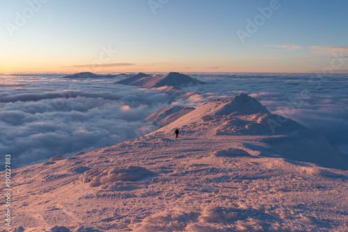 Man hiking on snow in Slovak mountains above clouds during sunset in winter