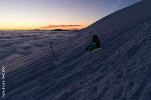 Hiking woman with headlamp on snow in Slovak mountains above clouds after sunset in winter