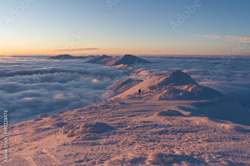Man hiking on snow in Slovak mountains above clouds during sunset in winter