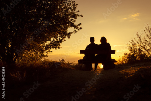 silhouette of a romantic couple sitting on a bench and watching the sunset on valentine's day