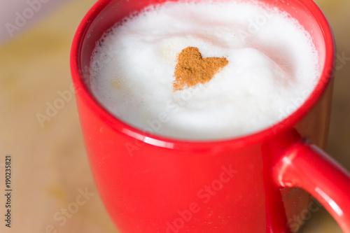 Heart of cinnamon powder on the milk froth of a latte in a red cup