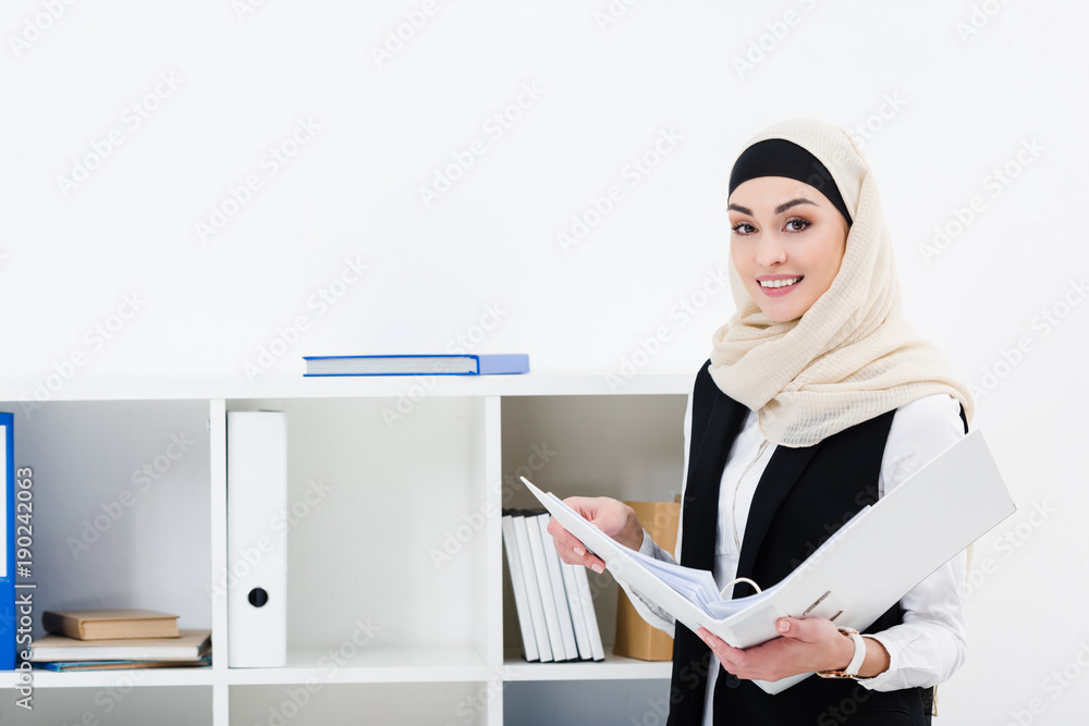 portrait of smiling businesswoman in hijab with folder in office portrait of smiling businesswoman in hijab with folder in office