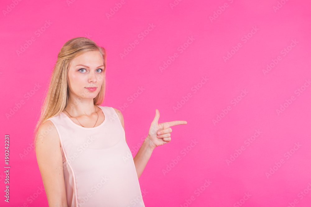 Young woman pointing at pink background with copy space Young woman pointing at pink background with copy space