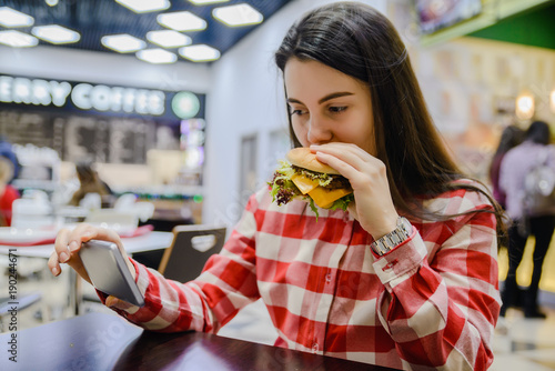 woman eat humburger while searfing the phone