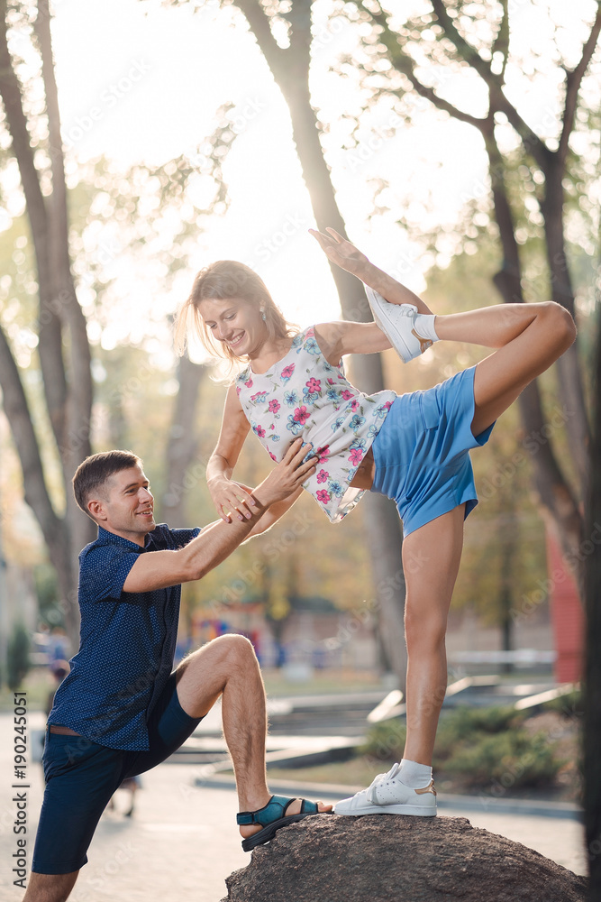 Fototapeta premium couple in love in the park, the guy helps the girl on the stone do yoga pose, laugh