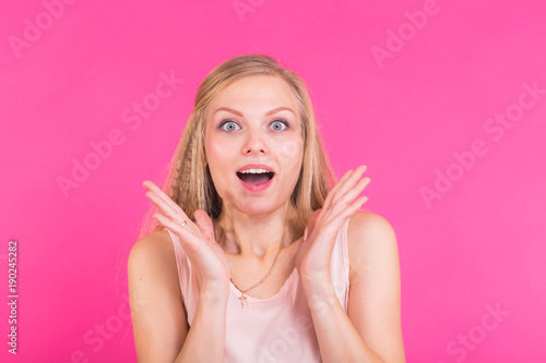 Surprised young woman over pink background. Looking at camera