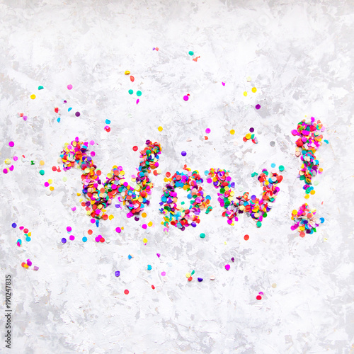 Word 'Wow!' made of colorful confetti on white textured background.