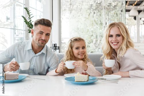 young family sitting in cafe and looking at camera