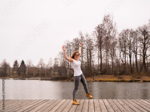 Junges Mädchen mit erhobenen Händen auf einem Holzsteg am See