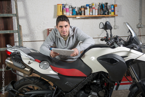 young man using a tablet next to motorcycle