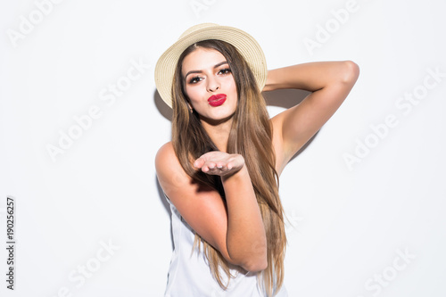 Beautiful young woman wearing summer straw hat blowing a kiss isolated on gray photo