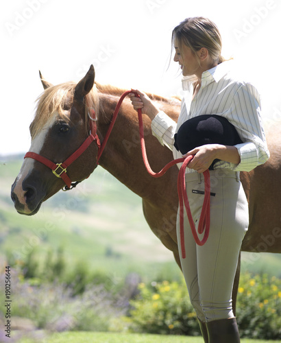 jokey lady walking with a brown horse with red reins