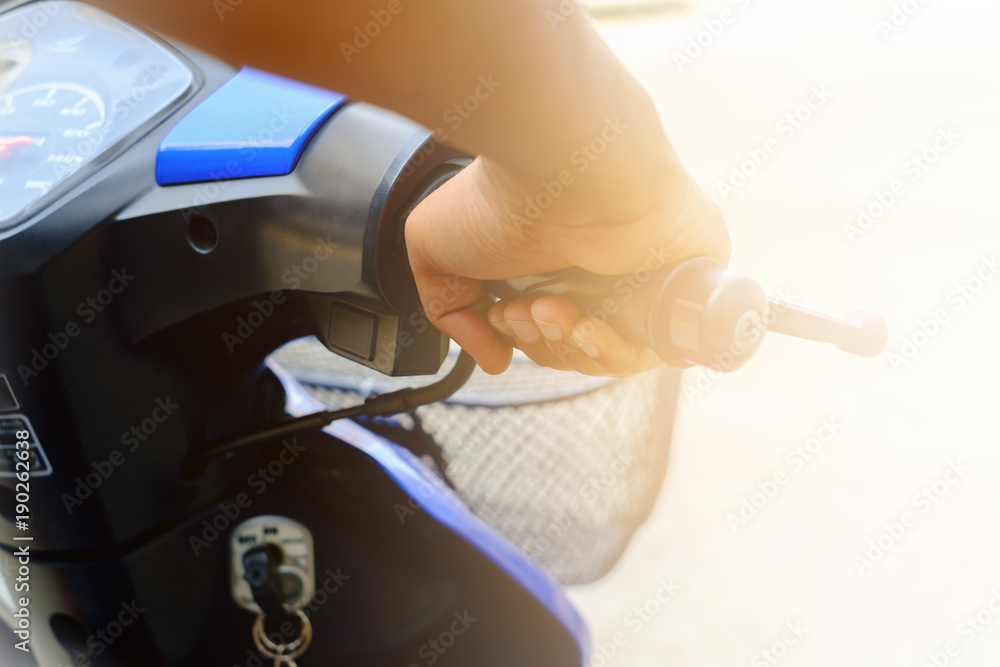 Selective focus of man's hand riding motorcycle on blurred concrete street road background with sun light effect for vehicle and transportation concept