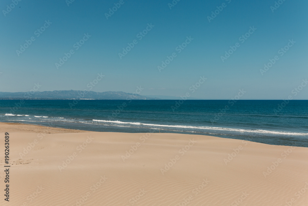 Imagen de paisaje soleado con dunas de arena y mar de fondo en cielo azul capturadas en Delta del Ebro en Cataluña