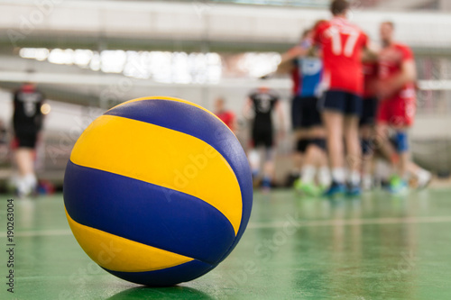 Yellow-blue volleyball on the floor in the gym, team of athletes is a bunch