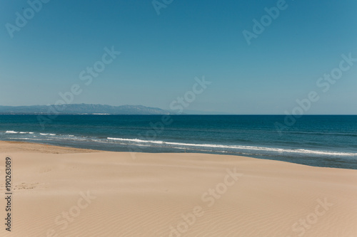 Imagen de paisaje soleado con dunas de arena y mar de fondo en cielo azul capturadas en Delta del Ebro en Catalu  a