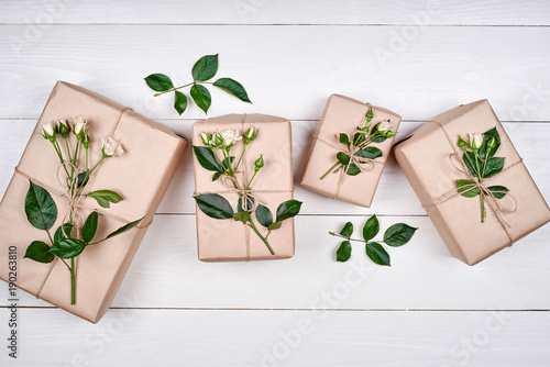 Gift boxes with branches of fresh roses on wooden table, copy space. Holiday background, sale, shopping. Gift wrapping. Greeting card for Valentines Day, Womans Day, Mothers Day, flat lay