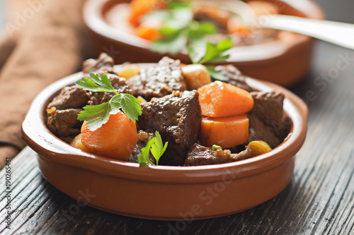 Slika na platnu Beef meat stewed with carrots and spices in ceramic pot  on old black wooden board