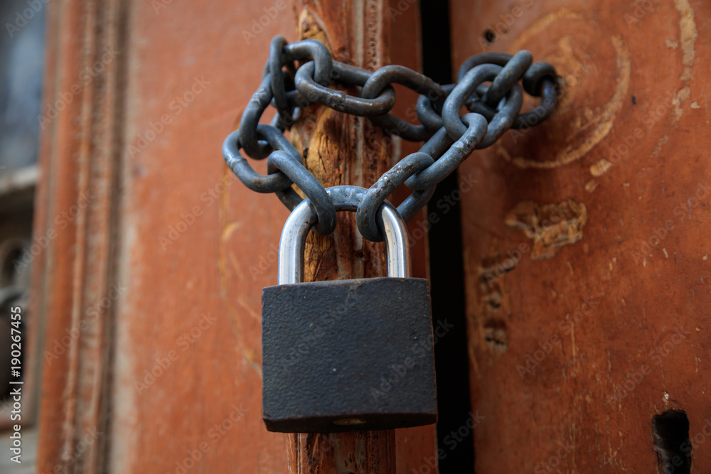 Wooden brown peeled door for background. Padlock with chain forbidden the entrance. Close up, detail