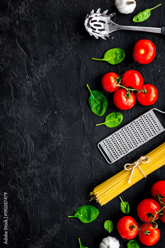 Italian pasta concept. Spaghetti, tomatoes, garlic, cheese grater, spoon for spaghetti on black background top view copy space