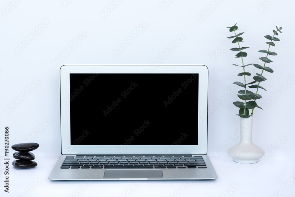 Fototapeta premium Modern Workspace with Laptop, Eucalyptus in Vase, Stacked Worry Stones