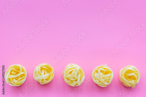 Uncooked tagliatelle. Italian pasta. Pattern on pastel pink background top view copy space