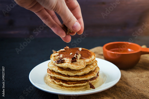 Female hand sprinkle with nuts Pancakes with honey