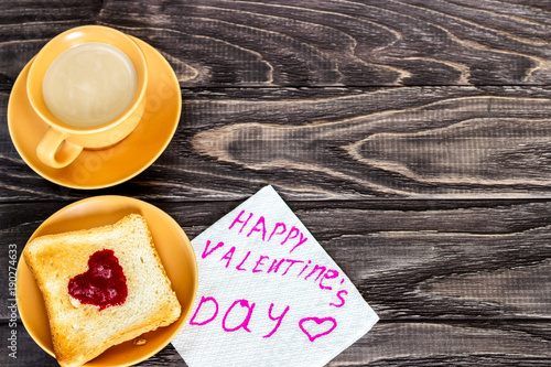 On a wooden background there is a cup of coffee with a toast on which a jam in the form of a heart. Valentine's day concept. photo