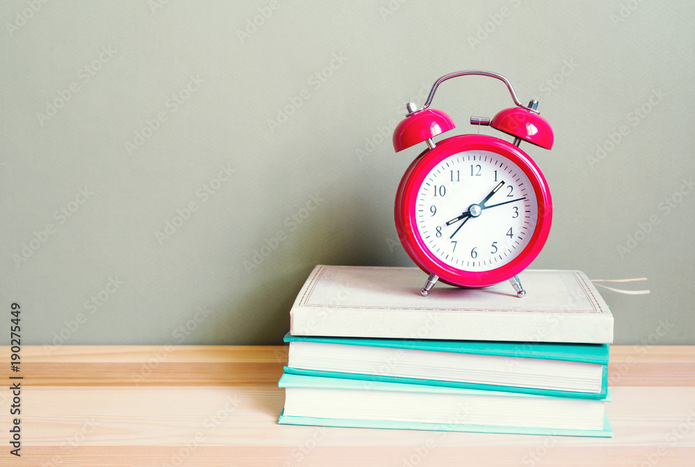 Red alarm clock shows time 08:07 and books on a wooden surface of a table. School background Red alarm clock shows time 08:07 and books on a wooden surface of a table. School background