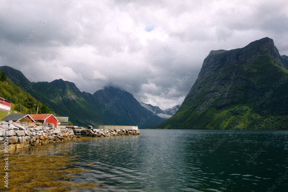 Picturesque scene of Urke village and Hjorundfjorden fjord, Norway. Drammatic sky and gloomy mountains panorama