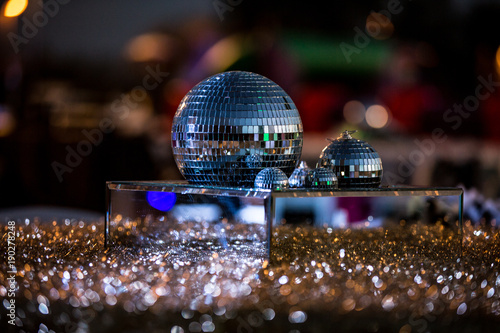 Mirrored disco balls on top of mirrored platform surrounded by glitter and jewels as centerpiece on table at party.