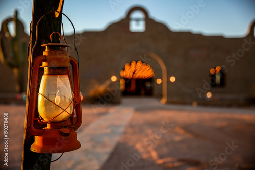 Old fashioned red Lantern hanging from post with adobe stucco building in background in desert. photo