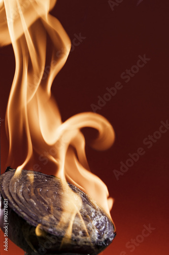 Red Onion on fire against deep red background. Close up with licking flames.