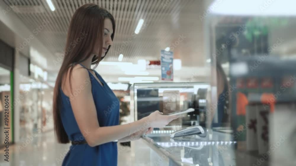 Woman brunette, fashion model shopping paying with NFC technology on mobile phone, in supermarket, mall airport terminal, student in dress credit card Woman brunette, fashion model shopping paying with NFC technology on mobile phone, in supermarket, mall airport terminal, student in dress credit card