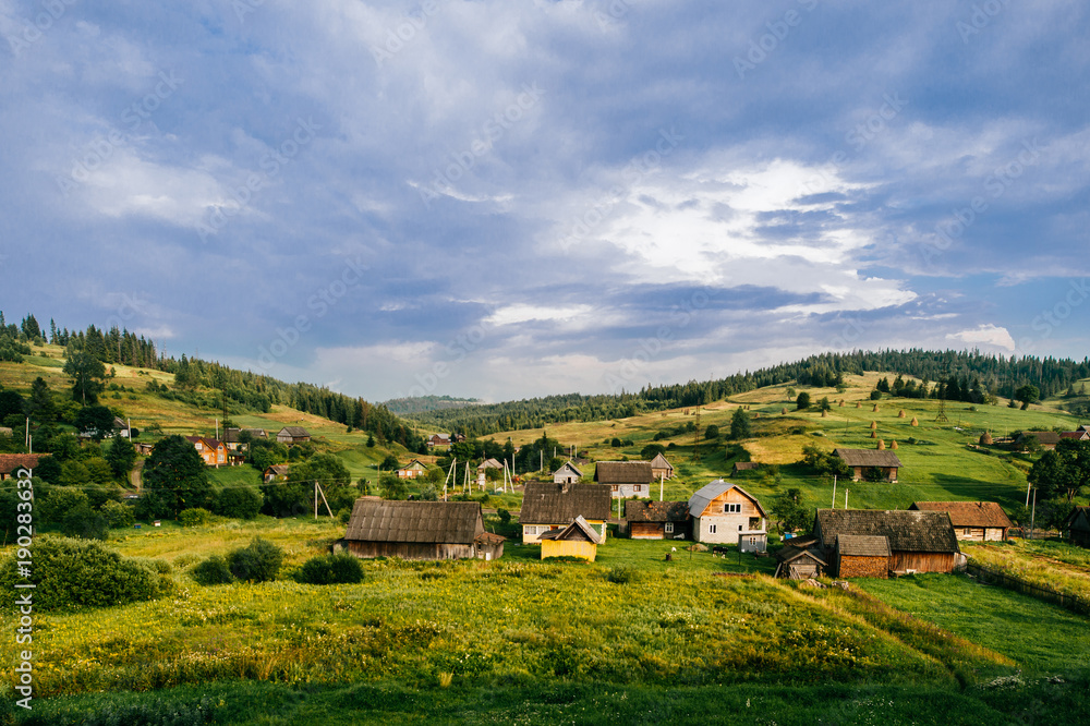 Countryside rural nature landscape in summer sunny day. Discover Ukraine. Village in Carpathians mountains. Beautiful scenic view at green hills and rustic terrain. Farmer houses in forest territory.