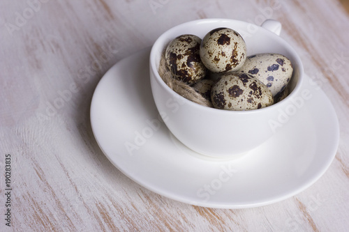 Quail eggs in a coffee cup and a bird nest with leaves on a white wooden background