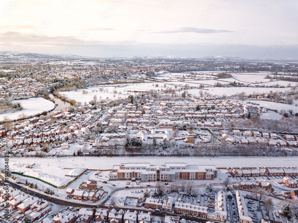 Fototapeta premium Aerial view of snow covered traditional housing suburbs in England. Snow, ice and adverse weather conditions bring things to a stand still in the housing estates of a British suburb