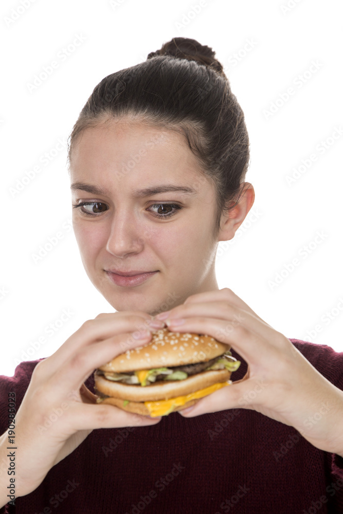 Adolescent girl looking suspiciously at a hamburger on a white background Adolescent girl looking suspiciously at a hamburger on a white background