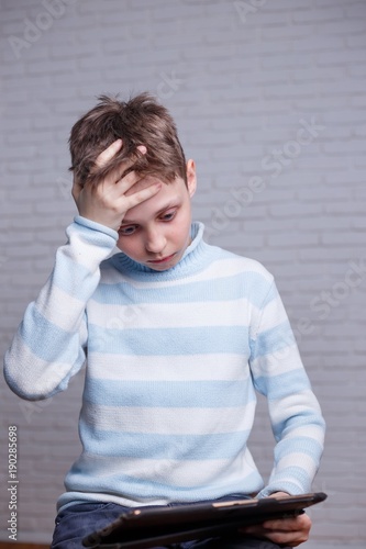 Upset frustrated boy with tablet. Gadget, internet addiction and technology concept photo