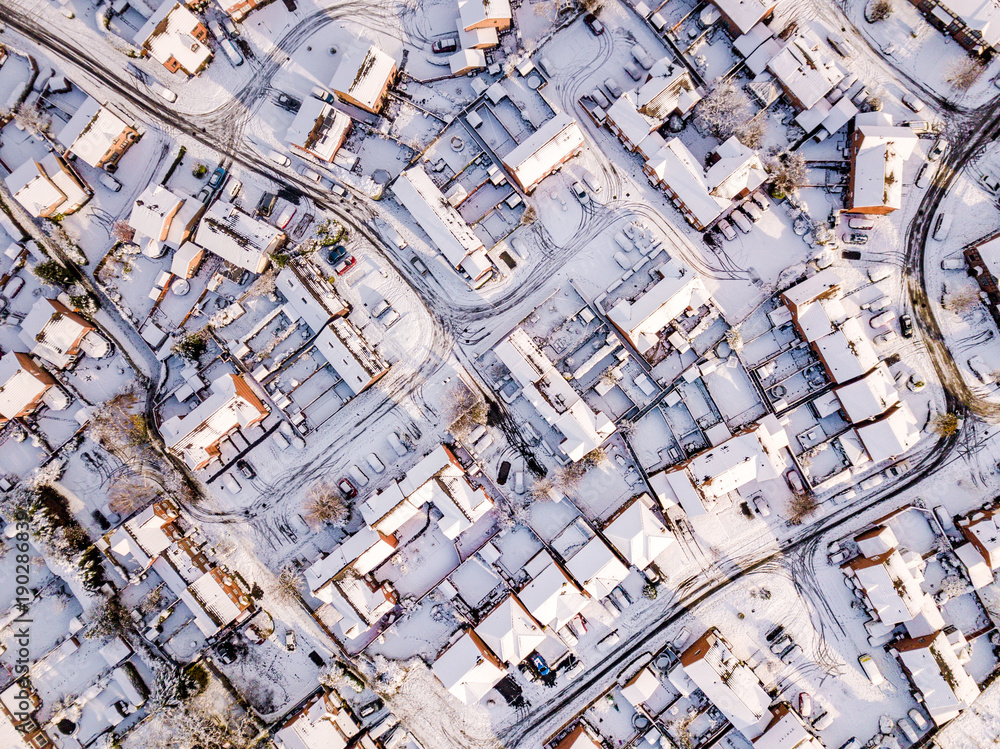Fototapeta premium Aerial view of snow covered traditional housing suburbs in England. Snow, ice and adverse weather conditions bring things to a stand still in the housing estates of a British suburb