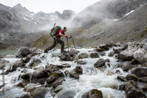 Hiker with large pack crossing a rocky river