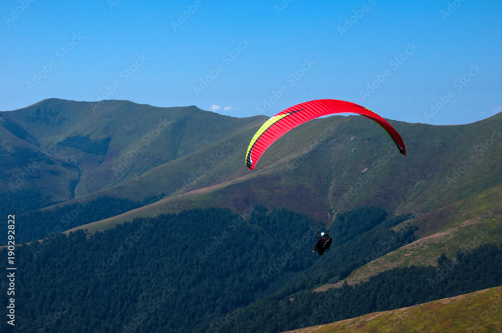 Paraglider flies over a mountain valley on a sunny summer day. Paragliding in the Carpathians in the summer. Paraglider flies over a mountain valley on a sunny summer day. Paragliding in the Carpathians in the summer.