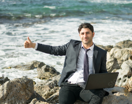 A man works on the beach far from the office. Freelancer and the worker are satisfied with the work.