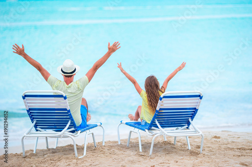 Father and daughter hands up on beach sitting on chaise-longue