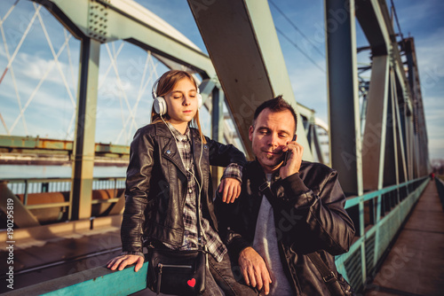 Father and daughter relaxing on bridge and listening music